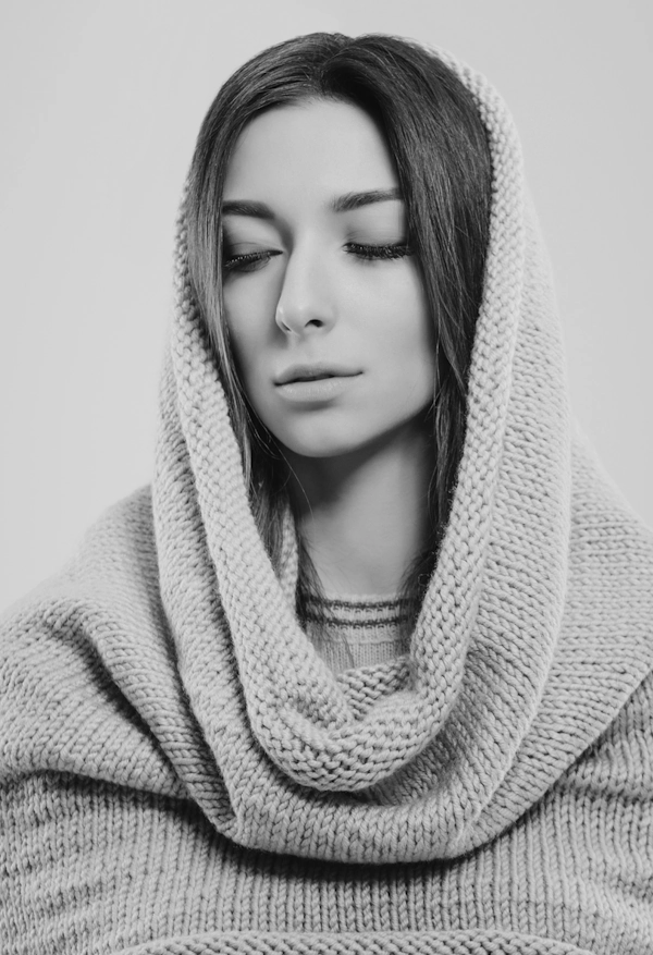 Жінка з м’якими рисами обличчя, закритими очима та рівним контуром підборіддя, одягнена у в'язаний светр із капюшоном — вигляд після естетичної процедури ліпосакції шиї